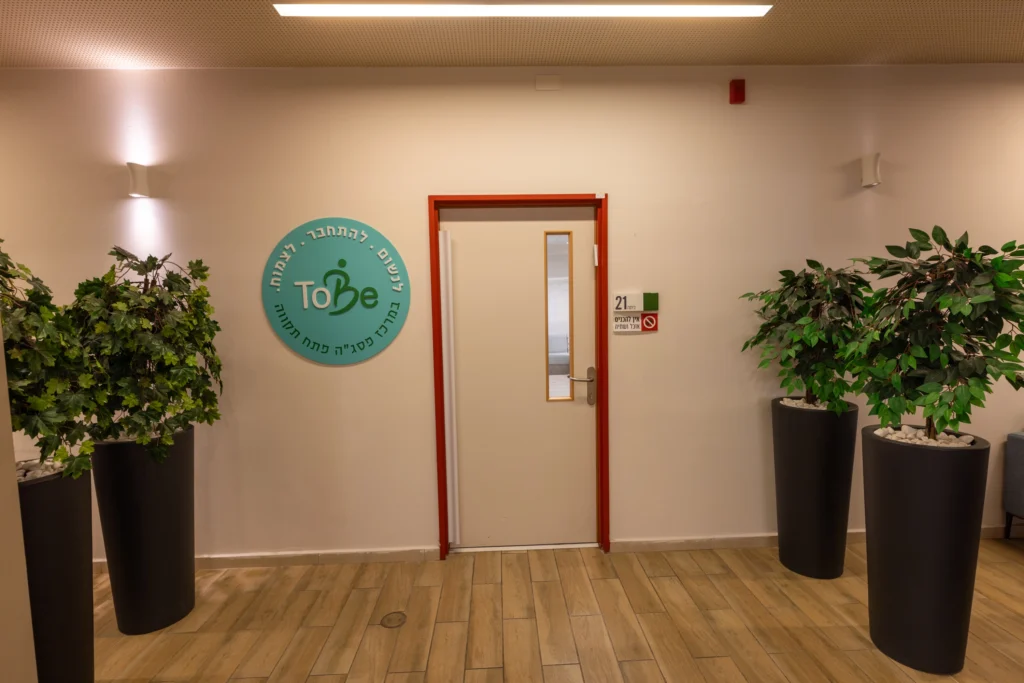 צילום של מבואת הכניסה למרכז To Be בפתח תקווה, עם שלט עגול על הקיר ועציצים.