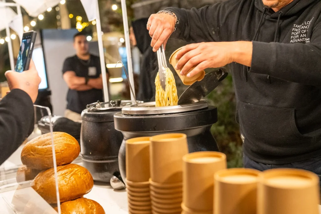 דוכן אוכל בפסטיבל האוכל בפתח תקווה מגיש מנת פסטה חמה בכוס נייר חומה.