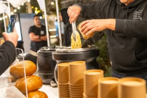 דוכן אוכל בפסטיבל האוכל בפתח תקווה מגיש מנת פסטה חמה בכוס נייר חומה.